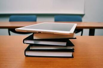 An iPad sits on top of a stack of books in a classroom.