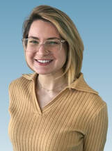 Head shot portrait of Amanda Jackey. She has blonde hair and is wearing a yellow collared sweater.