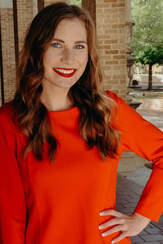 Sibbie Priestly stands outside smiling for a professional photo. She wears an orange dress with her left hand placed on her hip.