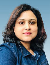 Head shot portrait of Malobika Bhattacharjee smiling. She has brown hair and is wearing a blue denim collared shirt.