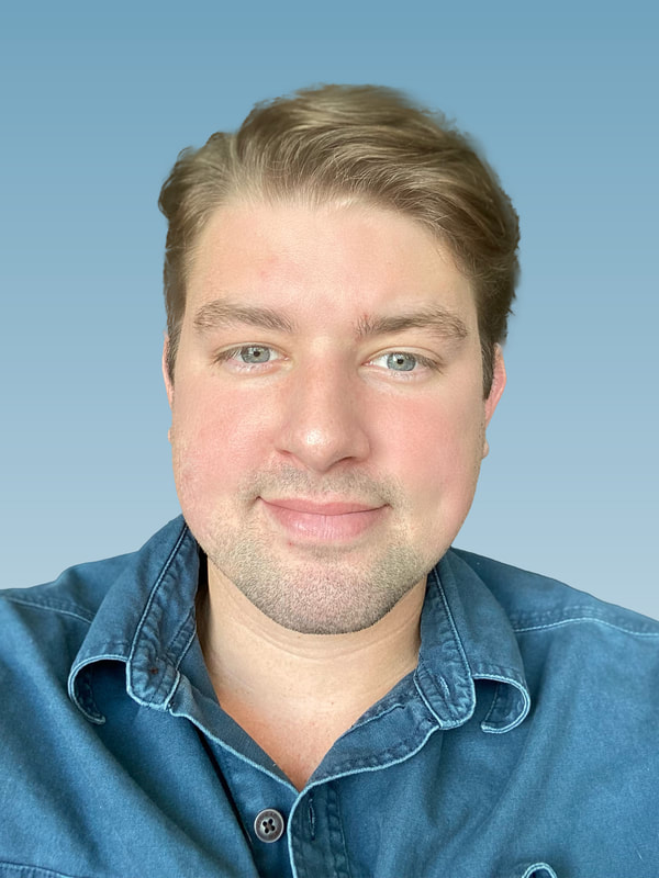 Head shot portrait of Sam Mancuso smiling. He has blonde hair and is wearing a blue denim collared shirt.