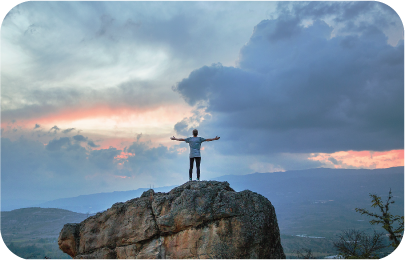 A man standing on a cliff at dusk with arms outstretched, showing success as a measurement of benchmark testing.